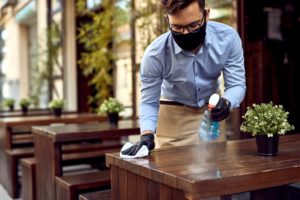 Man wearing a mask and gloves while wiping down a table at a restaurant due to COVID-19